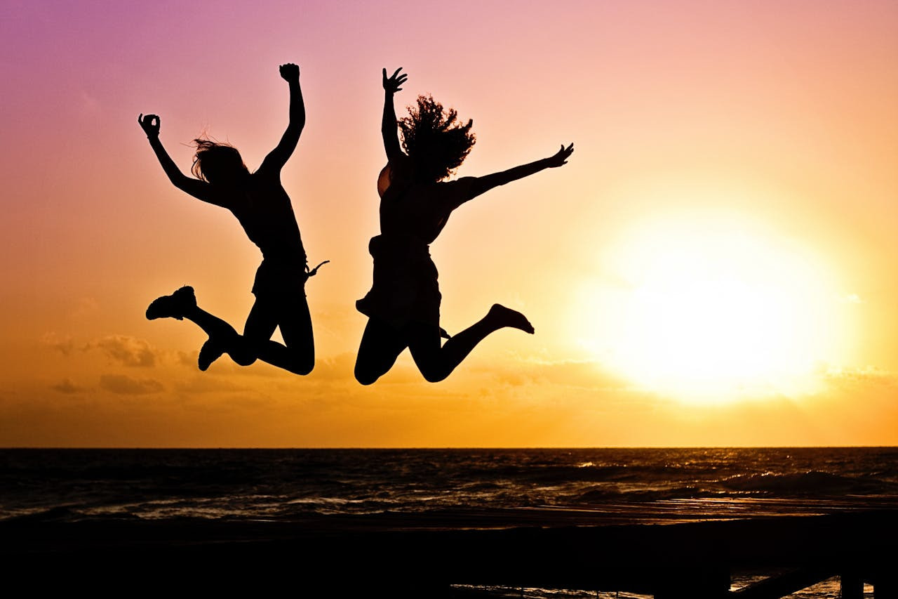Two silhouetted figures jump into the air against a rising sun, symbolizing energy, freedom, and self-activation.